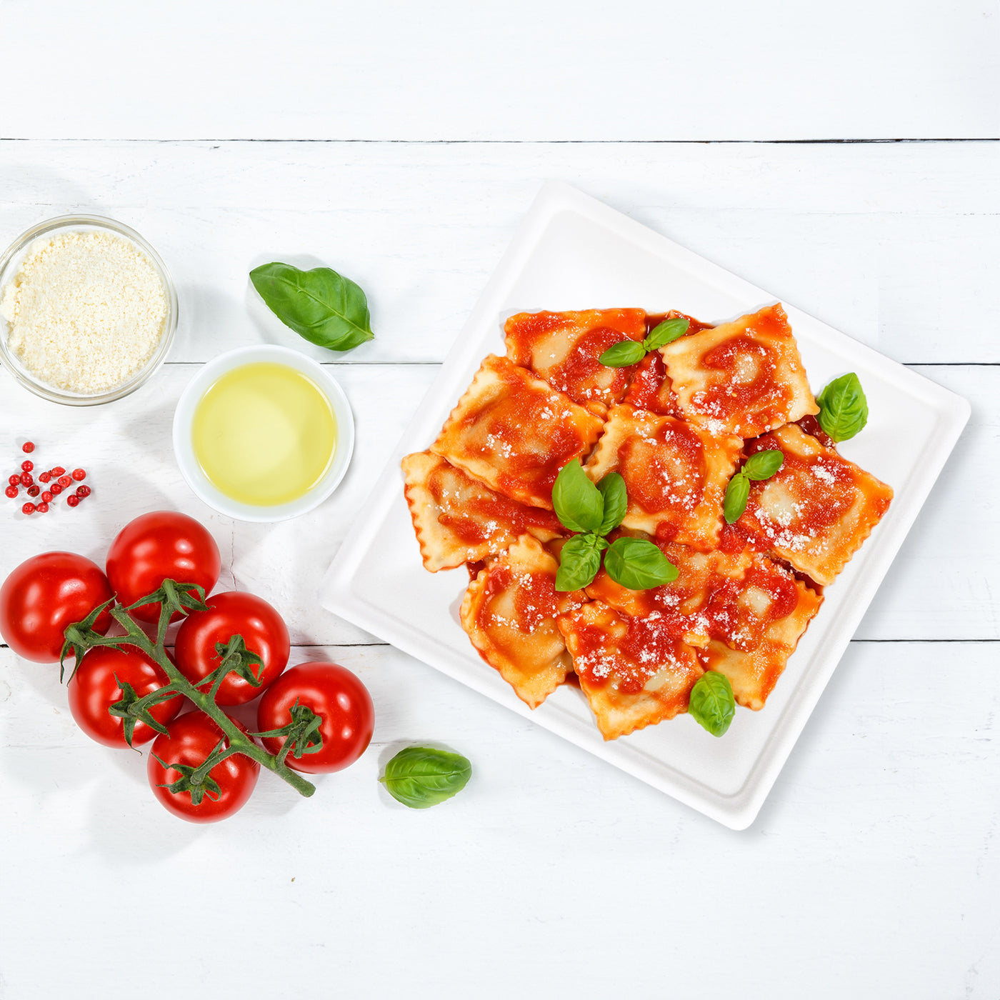 A plate of ravioli topped with tomato sauce and fresh basil leaves on a 10-inch square pearl white compostable plate.