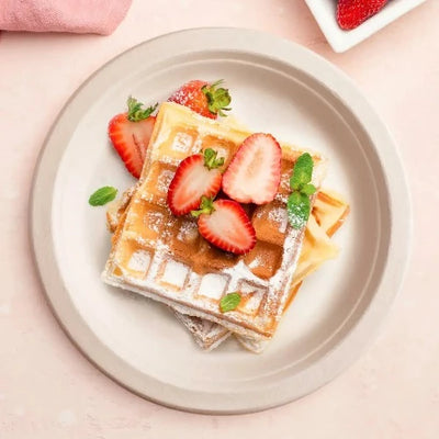 A plate with waffles and strawberries on it, served on a 9 Inch Round Compostable Plate.