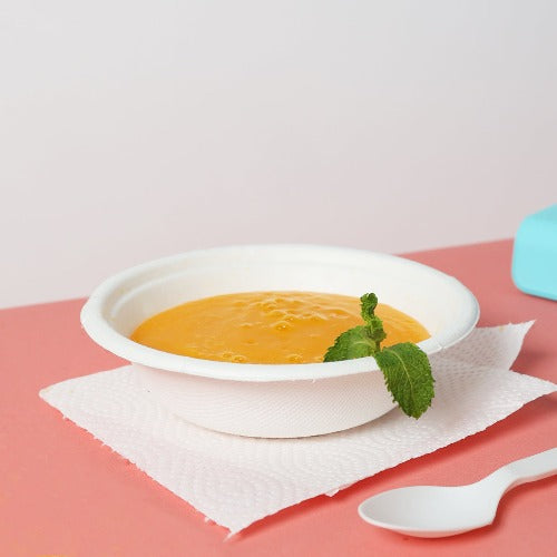 A bowl of soup with a spoon and a blue container, served in a 12 oz Pearl White Compostable Bowl.