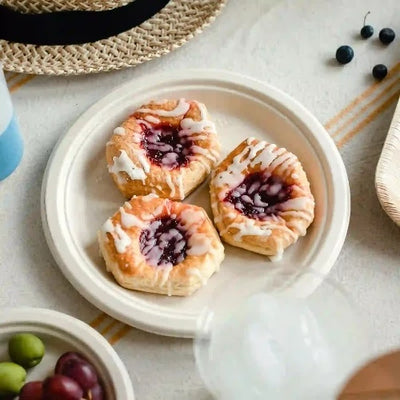 Three pastries on a plate with fruit and a straw hat. Served on 10 Inch Round Compostable Plates.