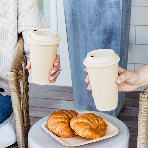 Two women enjoying coffee and croissants on a table, with 16oz compostable hot coffee cups and lids.