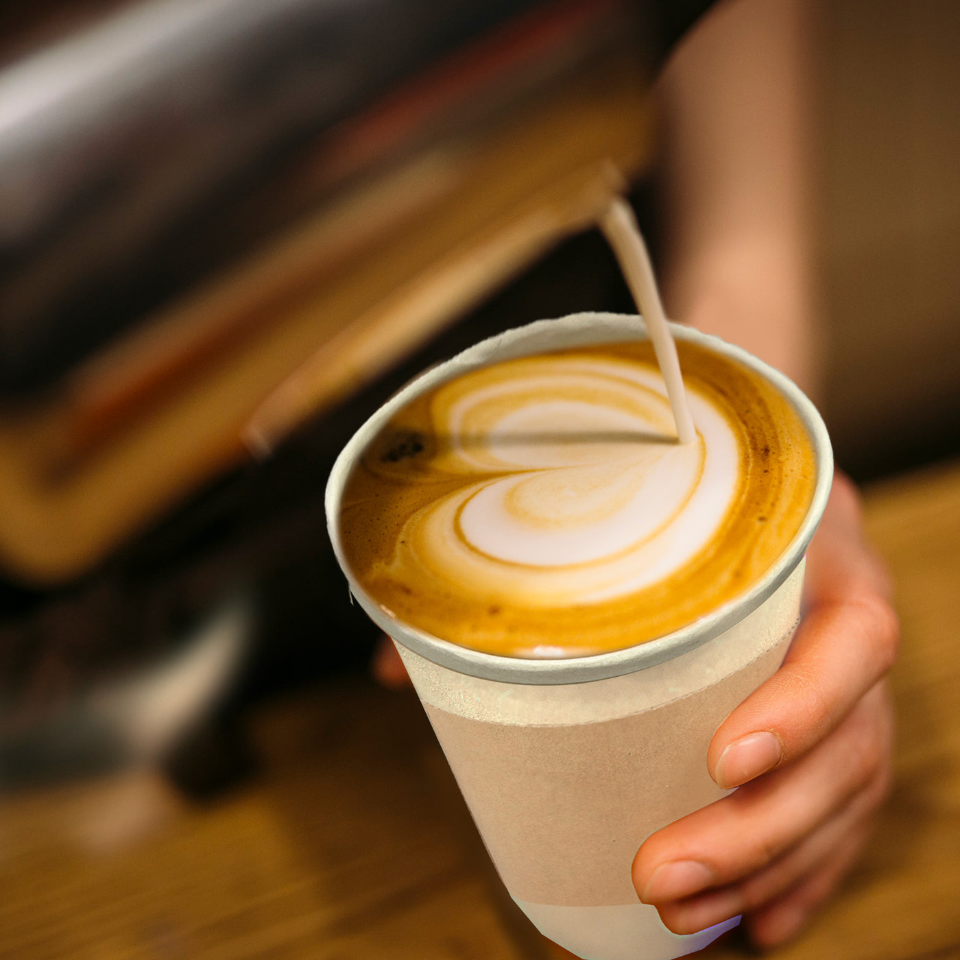 Person pouring latte into 16oz compostable hot coffee cup with lids and sleeves.