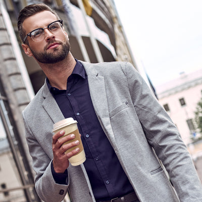 A man in glasses and a suit holding a coffee in a 12oz disposable cup with lids and sleeves.