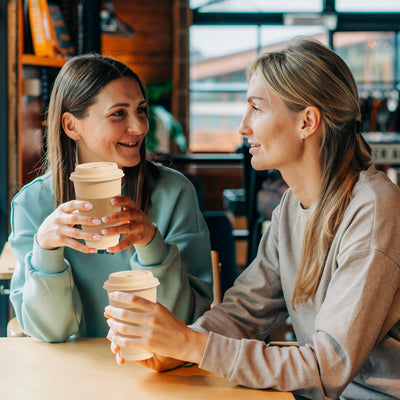 Two women sitting at a table, enjoying coffee in 16oz compostable hot coffee cups with lids and sleeves.