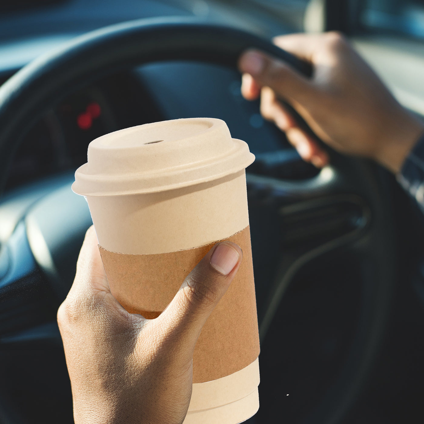 A person driving a car while holding a coffee cup. The cup is a 12oz disposable one with lids and sleeves.