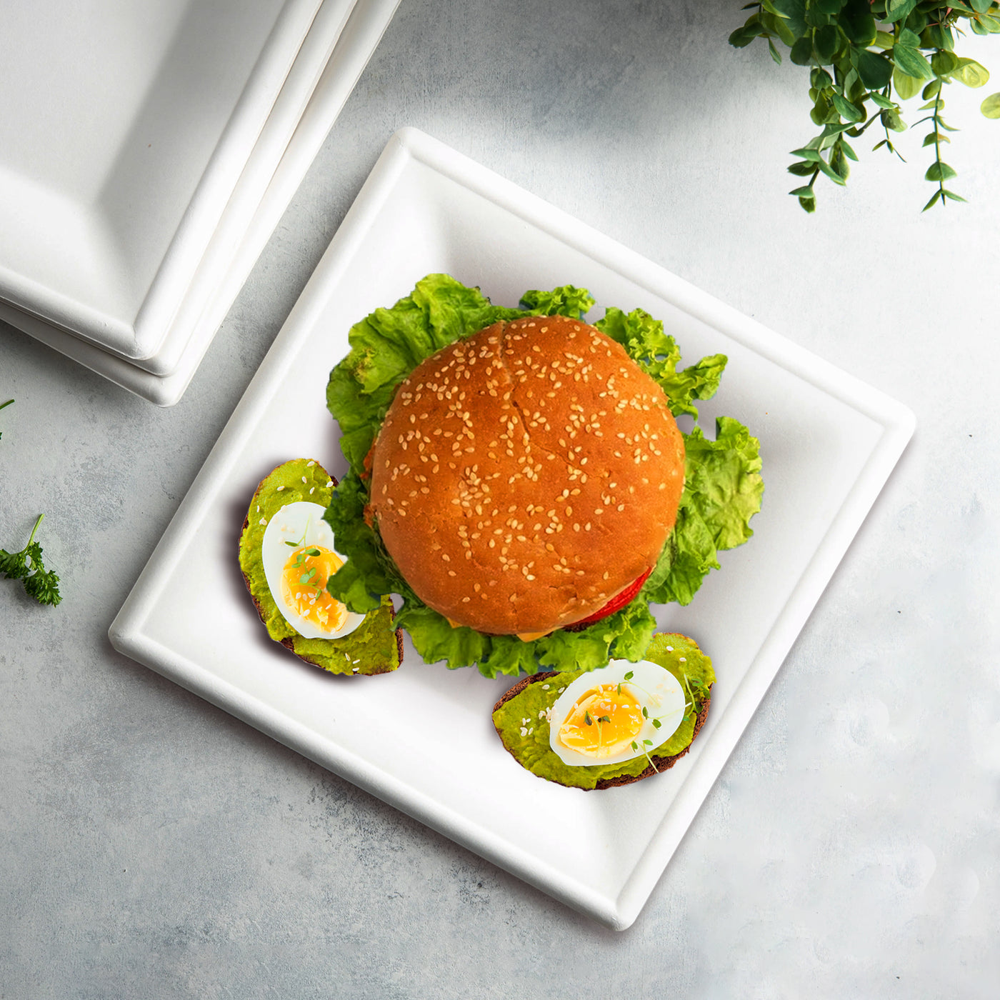 Hamburger topped with egg on a 6-inch square pearl white compostable plate.
