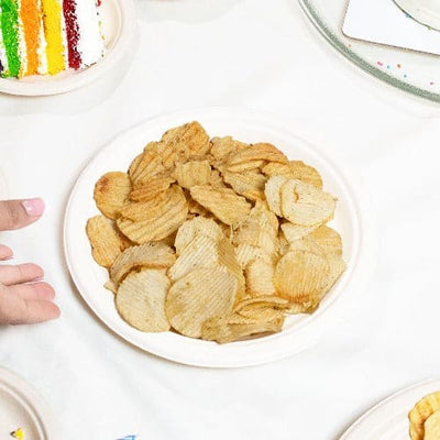 A table with a plate of chips and a cake on a 9 Inch Round Pearl White Compostable Plate.