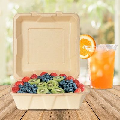 A 9 inch square compostable clamshell container filled with a variety of fruits and a refreshing orange drink.