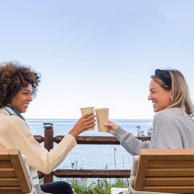Two women enjoying each other's company on a bench and having a cup of coffee on 12oz compostable Hot Chocolate Cups