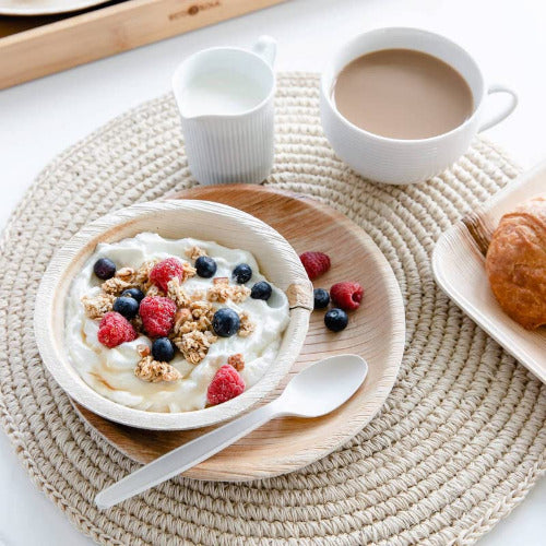 A delicious breakfast spread featuring yogurt with berries, croissants, compostable bowls and a set of compostable spoons.