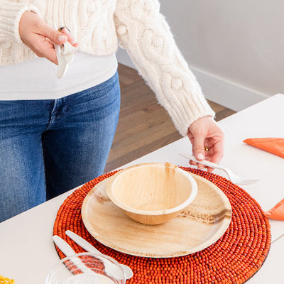 A woman arranging a  table with a Compostable Cutlery Set, Bowls and Plates