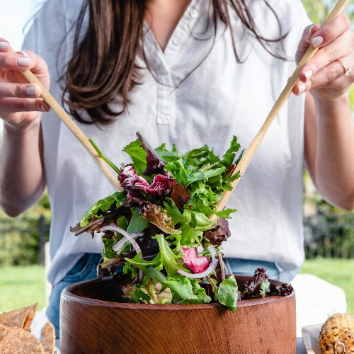 A woman holds a bamboo spatulas over a salad bowl 