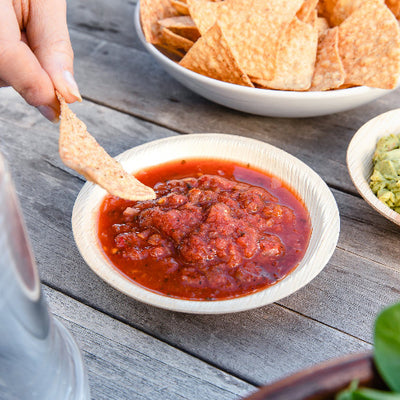 Dipping chips on sauce in 7 Oz compostable 5" round palm leaf bowls.